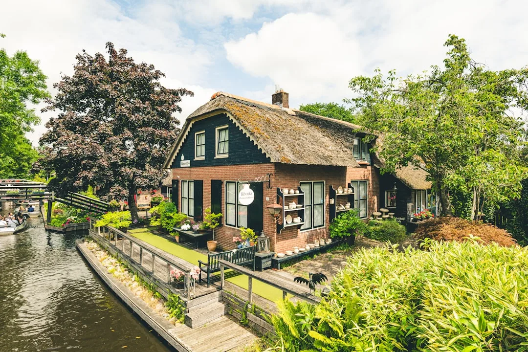 Verduurzaamde woning — Thatched roof house beside a canal with lush greenery.